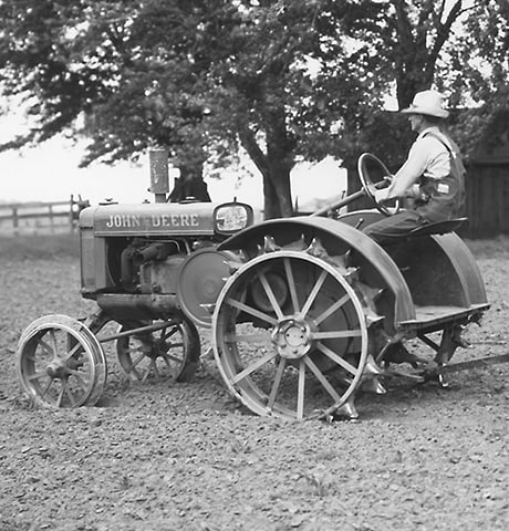 Historický univerzálny traktor "GP" spoločnosti John Deere ťahá za sebou po poli kultivátor John Deere č. 7.