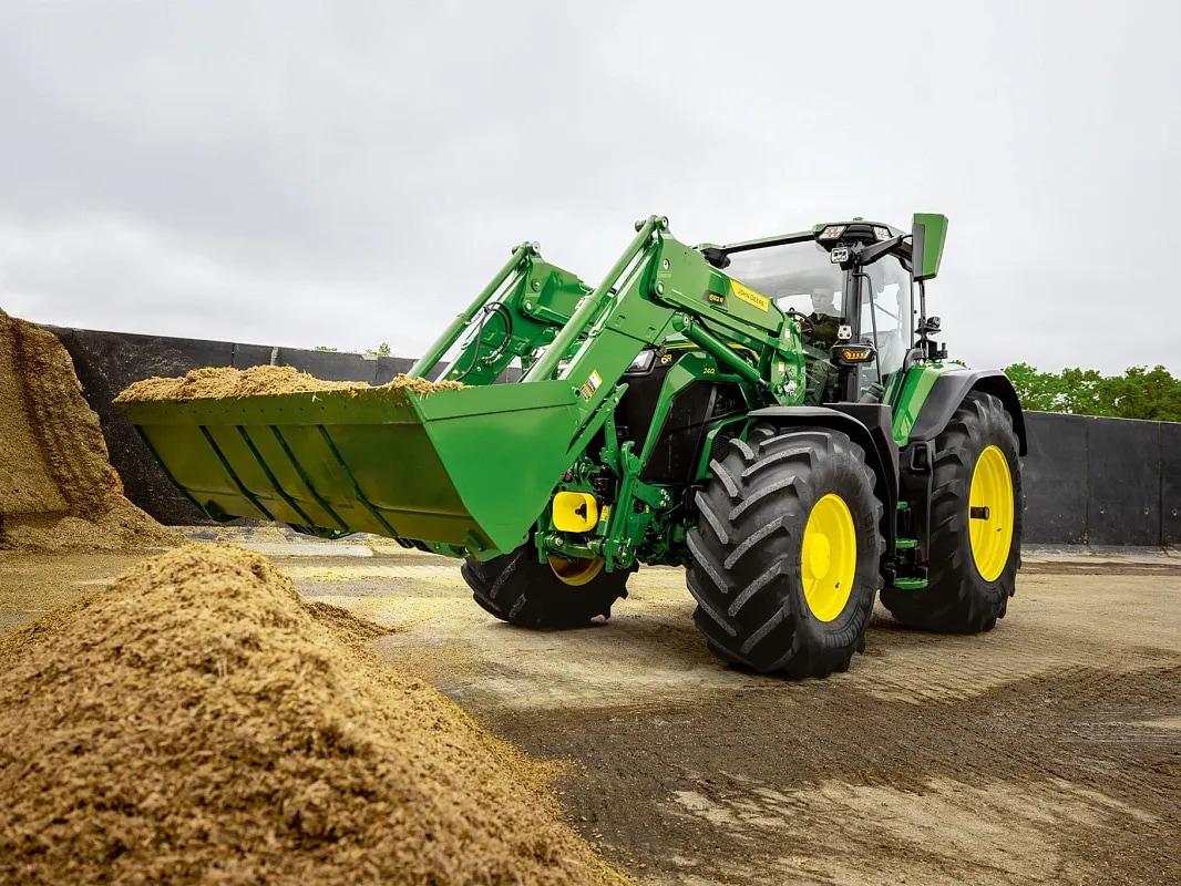 Lyžica čelného nakladača traktora John Deere naplnená silážou počas manipulácie s materiálom.