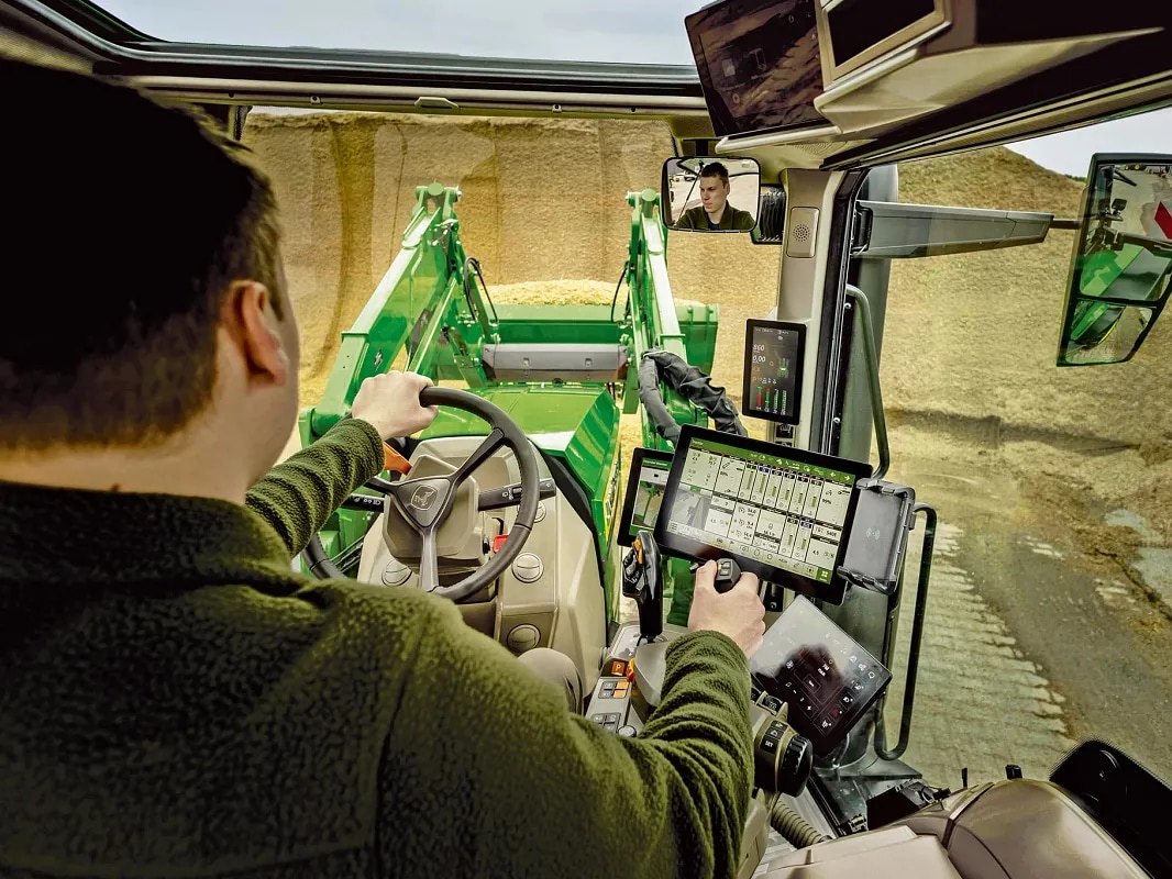 Pohľad z kabíny traktora John Deere zobrazujúci ovládacie prvky pre obsluhu a prácu s čelným nakladačom.