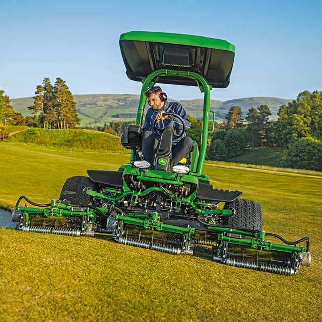 Čelný pohľad na správcu golfového ihriska, ktorý pracuje na trávniku so zelenou kosačkou John Deere.