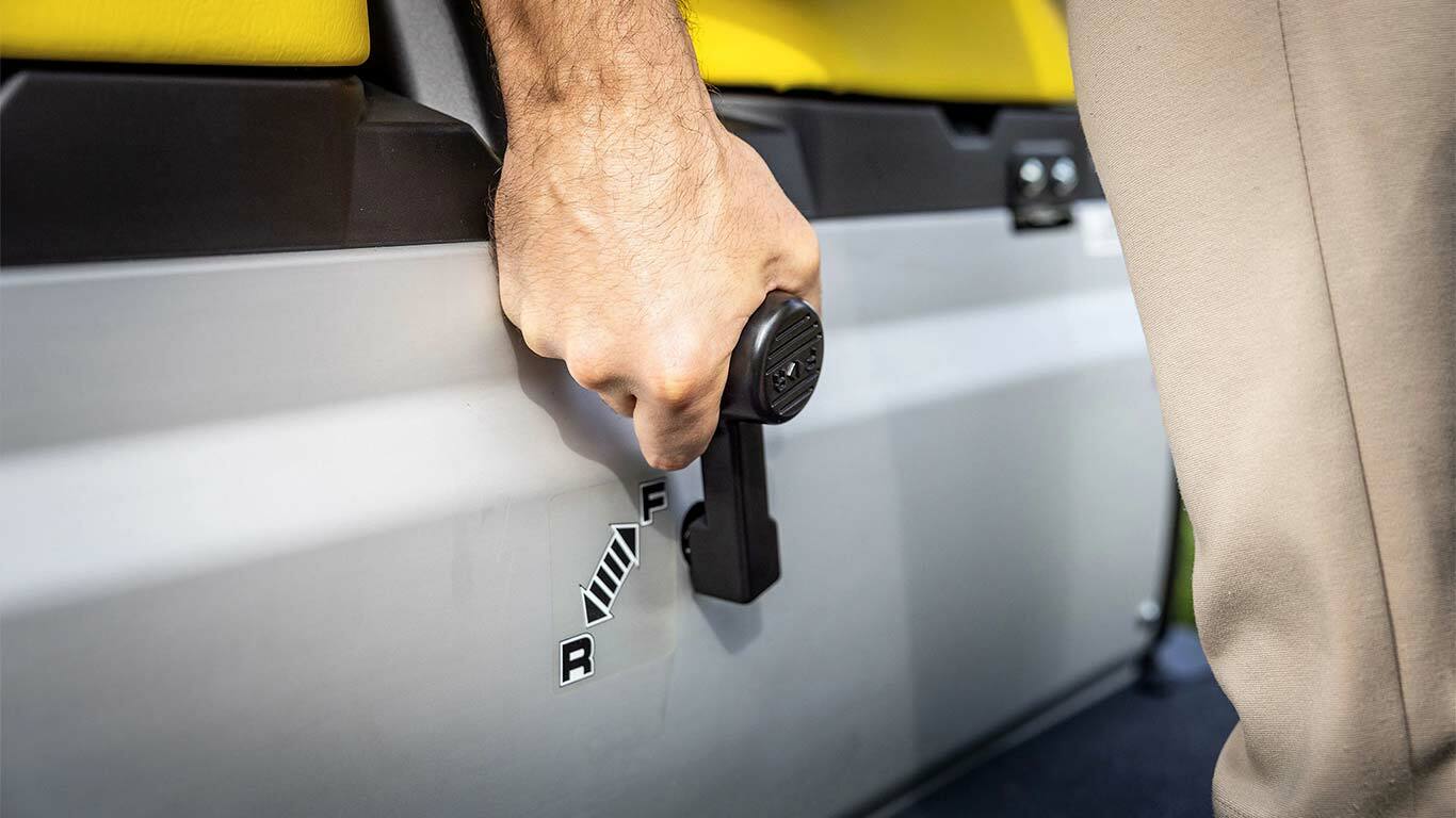 Detailný záber na ručné ovládanie páky radenia prevodov na vozidle Gator GS John Deere, zobrazujúci polohy jazdy vpred a vzad vedľa žltých sedadiel.