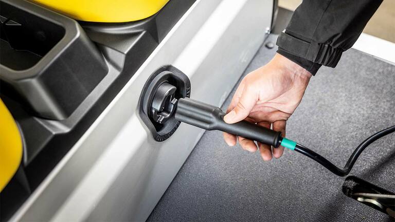 Ruka zapájajúca nabíjací kábel do bočného portu elektrického úžitkového vozidla John Deere Gator GS.