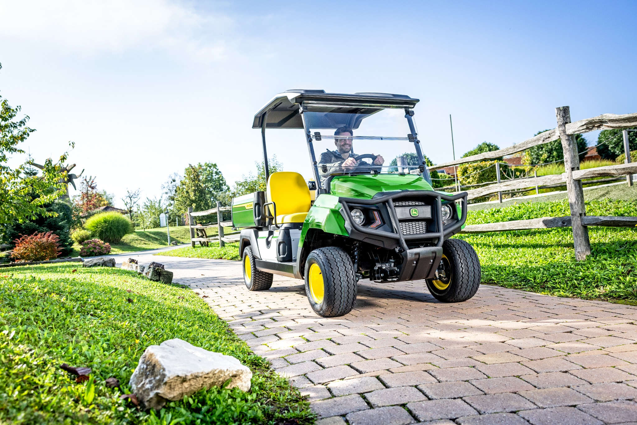 Úžitkové vozidlo Gator GS jazdiace po dláždenej ceste v upravenej oblasti Úžitkové vozidlo Gator GS jazdiace po dláždenej ceste v upravenej oblasti