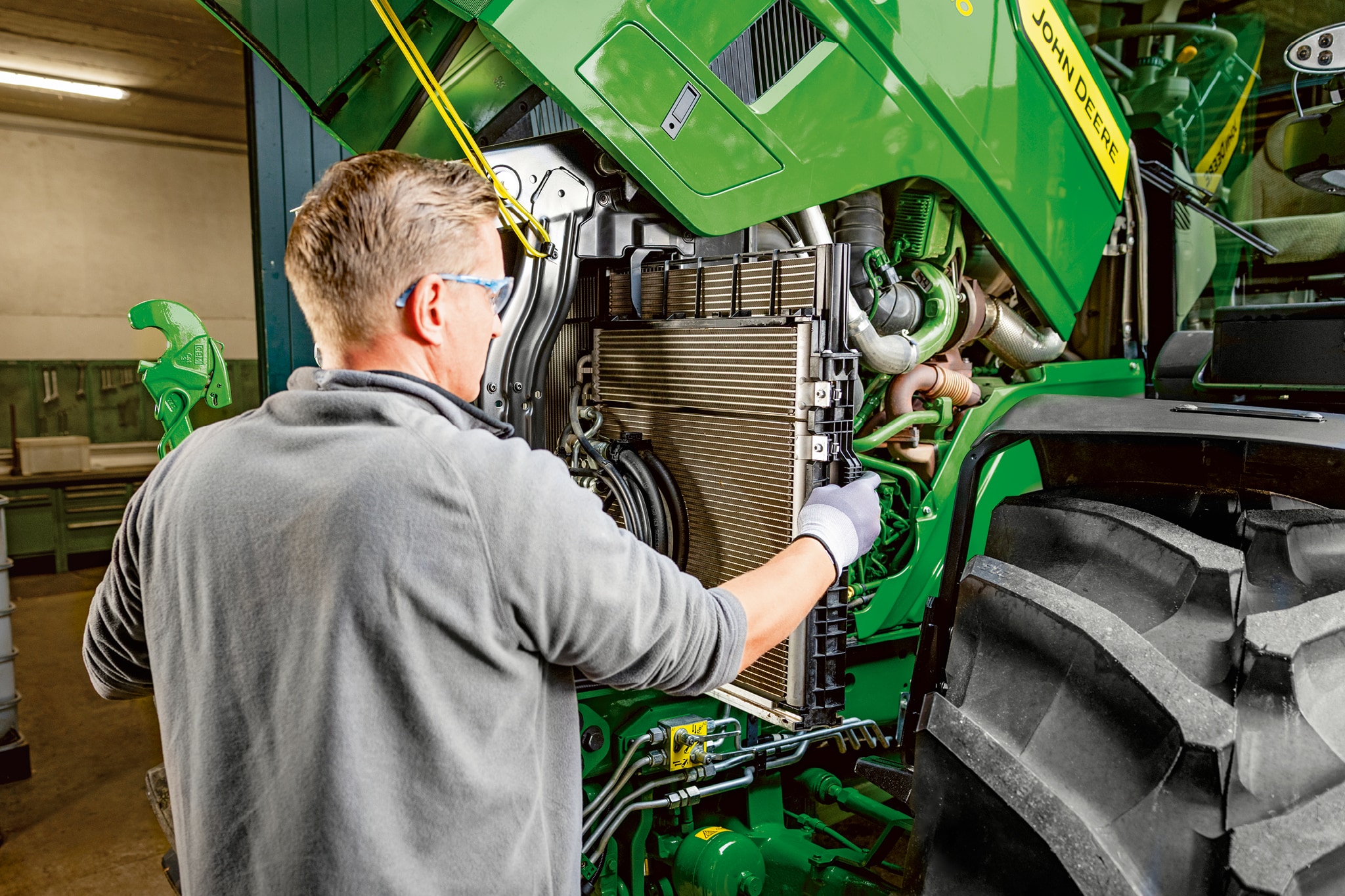 Servisný technik vykonávajúci údržbu v motorovom priestore traktora John Deere radu 6M.