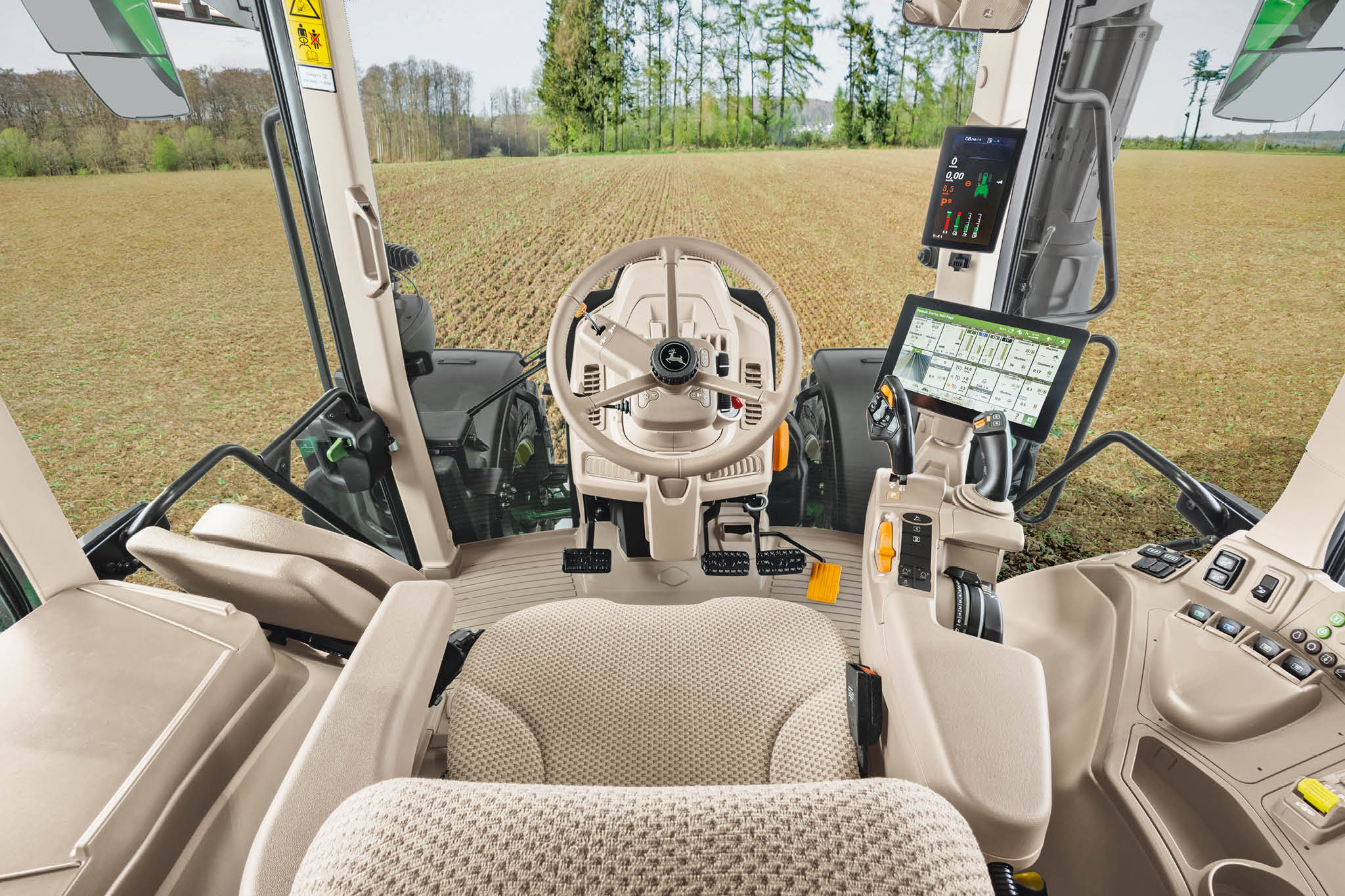 Prehľad interiéru kabíny traktora John Deere radu 6M so sedadlom vodiča, volantom a digitálnymi displejmi.