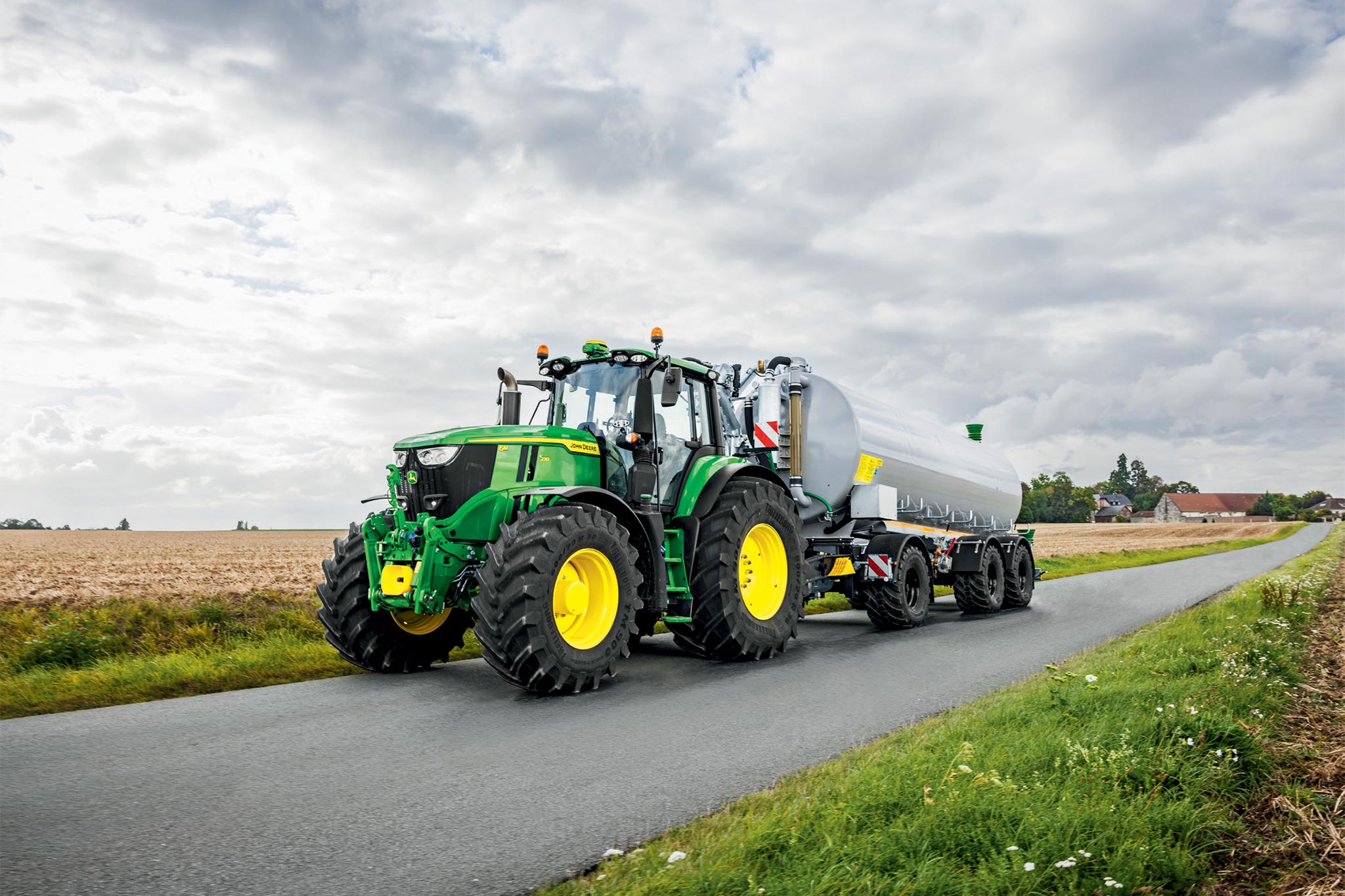 Pohľad zhora na traktor John Deere série 6M pracujúci na poli po zbere so širokým kultivačným zariadením a prašnou stopou.