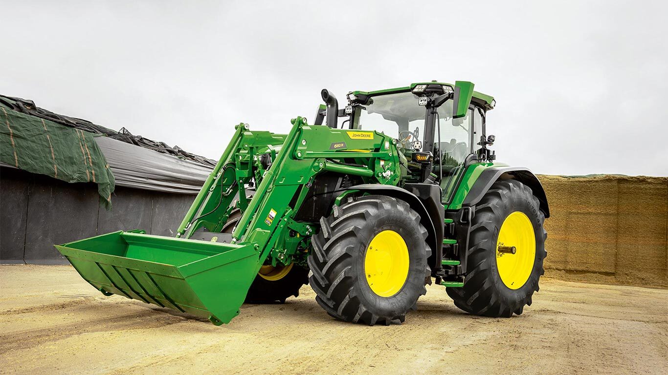 Traktor John Deere s čelným nakladačom zaparkovaný na dvore farmy v blízkosti skladiska siláže.