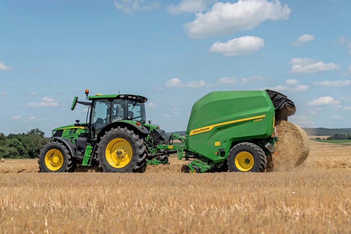 John Deere V452R na slamenom poli ťahaný traktorom John Deere 6R 150 vyhadzuje balík