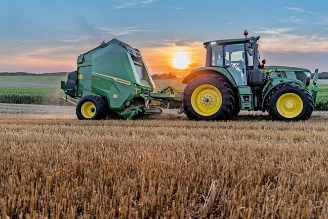 John Deere V462M na slamenom poli ťahaný traktorom John Deere 6M 150 pri západe slnka