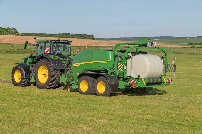 Zvinovací lis John Deere C442R ťahaný traktorom John Deere 6R 185, ktorý vyrába vysokohustotné silážne balíky