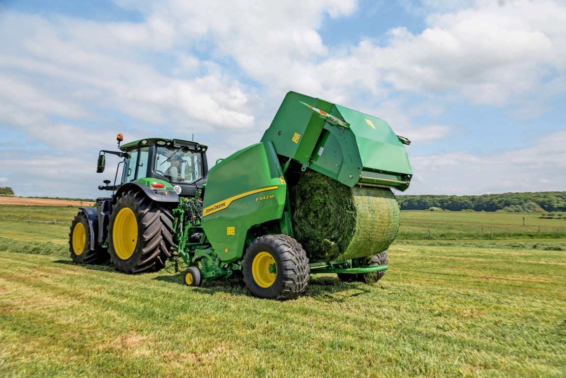 John Deere F442M lis na balíky ťahaný traktorom John Deere 6M, ktorý vyhadzuje balíky trávy