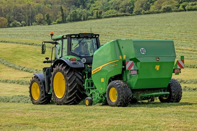 John Deere F442M lis na balíky ťahaný traktorom John Deere 6M na kopcovitom trávnatom poli