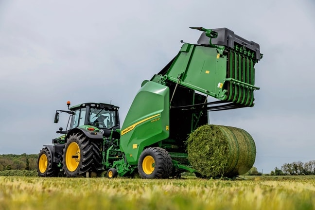 Lis na balíky John Deere V462M ťahaný traktorom John Deere 6M, ktorý vyhadzuje balík trávy