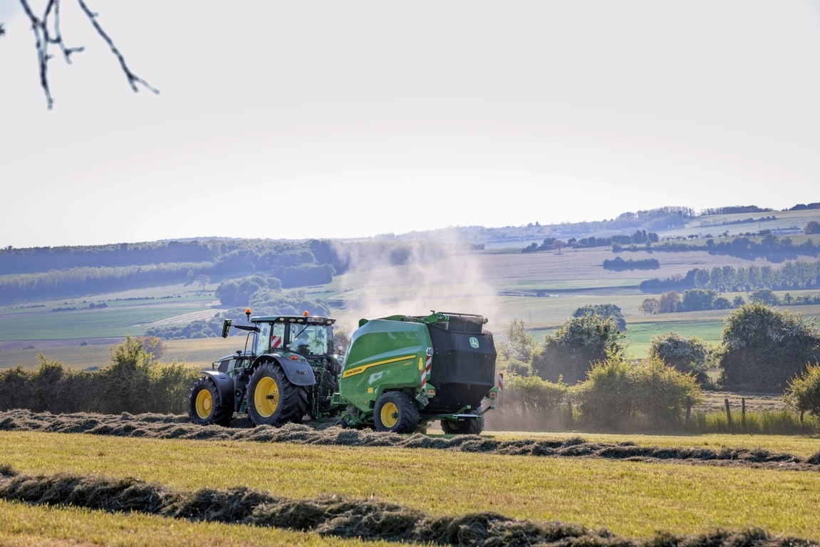 John Deere V462R ťahaný traktorom John Deere 6R 185, ktorý lisuje seno